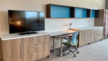 A modern office space with a flat-screen TV, a desk with a chair, and built-in shelving.