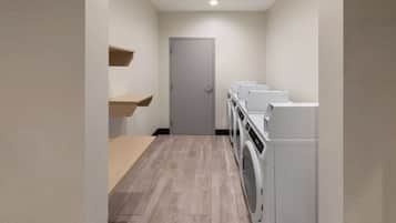 A laundry room with a door, wooden shelves, and a row of washing machines.
