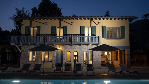 A two-story building with a pool, outdoor seating, and a balcony with umbrellas. - Villa Laura (Gardone Riviera)