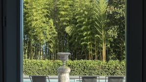 A view through a door of a pool area with a stone fountain, lounge chairs, and a forested background. - Villa Laura (Gardone Riviera)