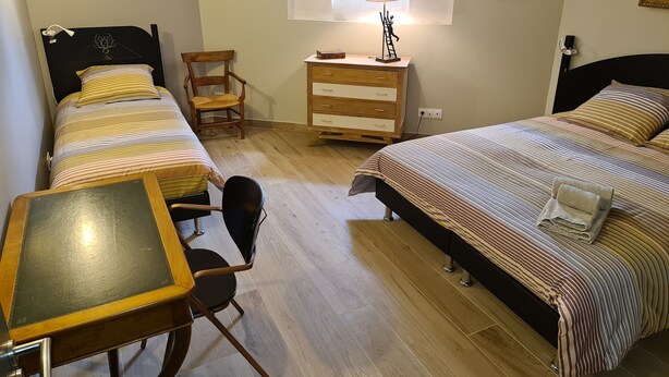 A bedroom with two beds, a desk, a chair, a dresser, and a window with a lamp.