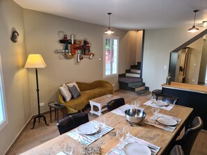 A dining area with a wooden table set for four, a sofa, and a staircase in the background.