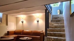 A living room with a brown leather sofa, two round tables, a stone staircase, and wall-mounted lighting.
