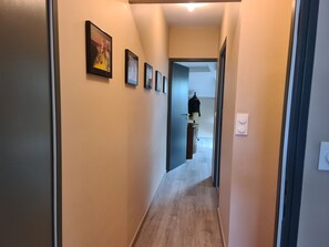 A narrow hallway with light-colored walls and a wooden floor. There are several framed pictures on the wall.