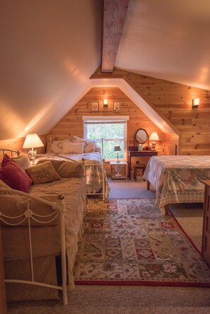 Cozy attic bedroom with two beds, a desk, and a window.