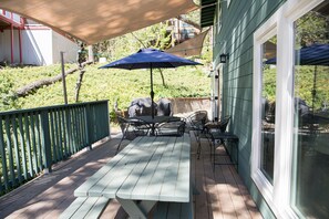 Eine Holzterrasse mit Picknicktisch und -stühlen, einem blauen Sonnenschirm und einem grünen Zaun.