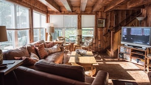 Un salón acogedor con interior de madera, un sofá de cuero, una mesa de centro y un televisor sobre un mueble de madera.
