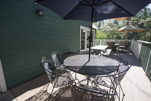 Eine überdachte Terrasse mit rundem Tisch, Stühlen, einem Grill und Blick auf die umliegenden Bäume.