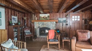 Una sala de estar acogedora con paredes de madera y una chimenea de piedra. Hay dos sofás de cuero, una silla de madera y una pequeña mesa.
