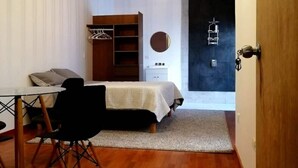 A compact bedroom with a bed, bedside table, chair, wardrobe, and a hanging light fixture. - Executive Studio - 15 min. from US Consulate | Flexible Check-in (Ciudad Juárez)