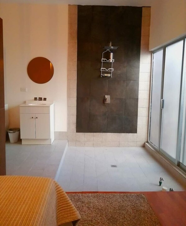 A modern bathroom with a large dark tiled wall, a white sink, and a mirror. - Executive Studio - 15 min. from US Consulate | Flexible Check-in (Ciudad Juárez)