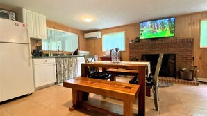 Una cocina con una mesa y un banco de madera, un televisor sobre la chimenea y un refrigerador.