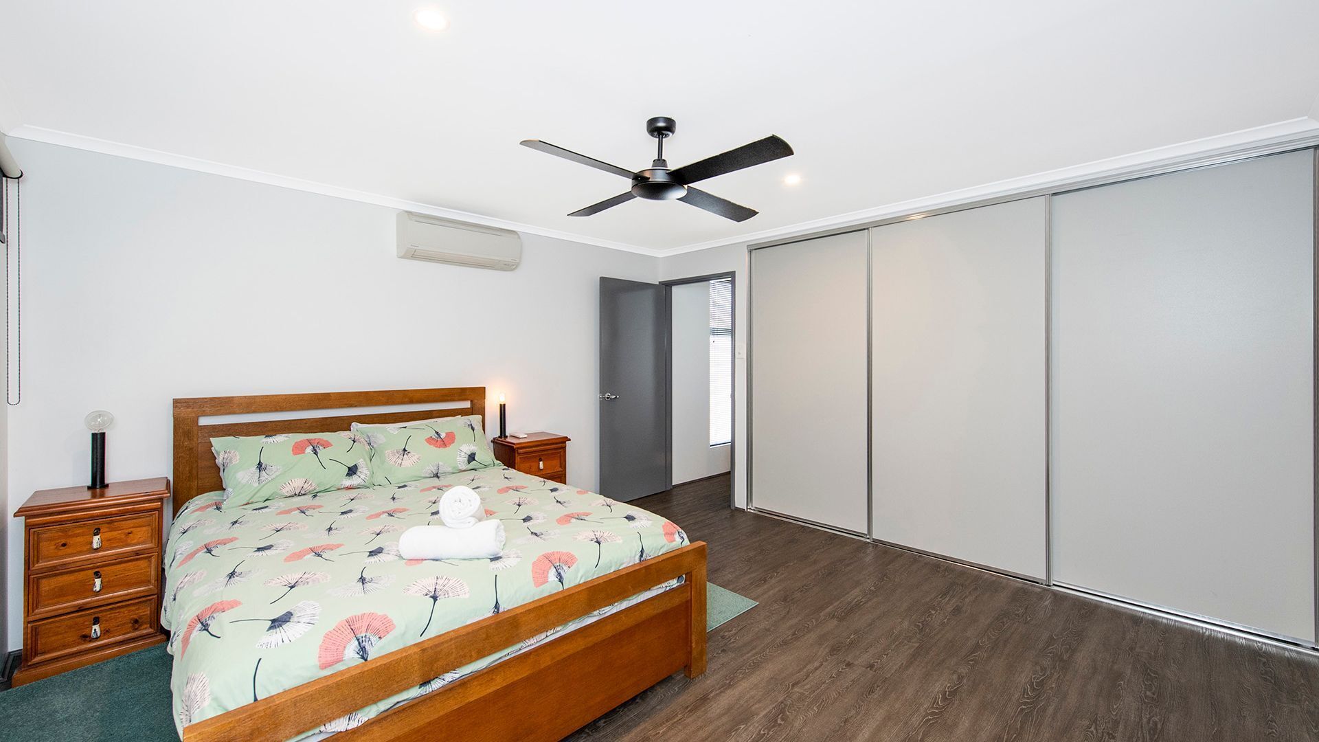 A bedroom with a wooden bed, a ceiling fan, a bedside table with a lamp, and a wardrobe.