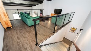 A modern interior with a staircase, wooden flooring, a green sofa, and a glass railing. - Vasse New-Yorker Townhouse (KEALY)