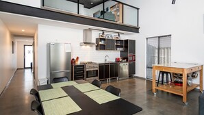 A modern kitchen with a dining area, featuring a stainless steel refrigerator, oven, microwave, and a wooden table with chairs. - Vasse New-Yorker Townhouse (KEALY)