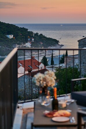 Ein Balkon mit Esstisch, mit Blick auf eine Küstenstadt, Gebäude und das Meer.