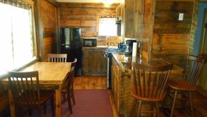 A wooden cabin interior with a dining table, chairs, a refrigerator, a microwave, and a sink. - Post and beam cabin with bunk beds (Shirley Mills)