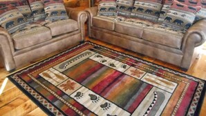 A cozy living room with a brown sofa set, patterned cushions, and a colorful area rug. - Post and beam cabin with bunk beds (Shirley Mills)