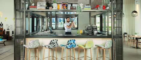 Une cuisine moderne avec un coin bar, où l’on voit une personne prendre une photo, des tabourets de bar et divers appareils de cuisine.