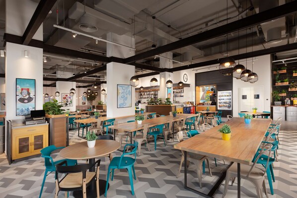 A modern cafe with multiple tables and chairs, indoor plants, and artwork on the walls. - Rove City Walk (Dubai)
