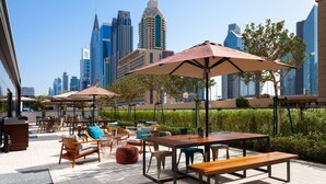 An outdoor seating area with tables and chairs, umbrellas, and a city skyline in the background. - Rove City Walk (Dubai)