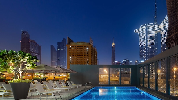 A rooftop swimming pool with lounge chairs and a view of city skyscrapers at night. - Rove City Walk (Dubai)