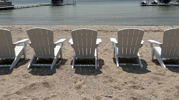 Une plage où l’on a disposé en rangée des chaises Adirondack blanches, toutes orientées vers la mer.