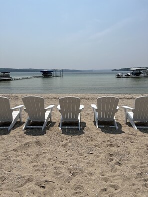 A beach with white Adirondack chairs lined up facing the water. - North Lake Leelanau carriage/cottage. Sandy beach front on North Lake Leelanau. (Leland)