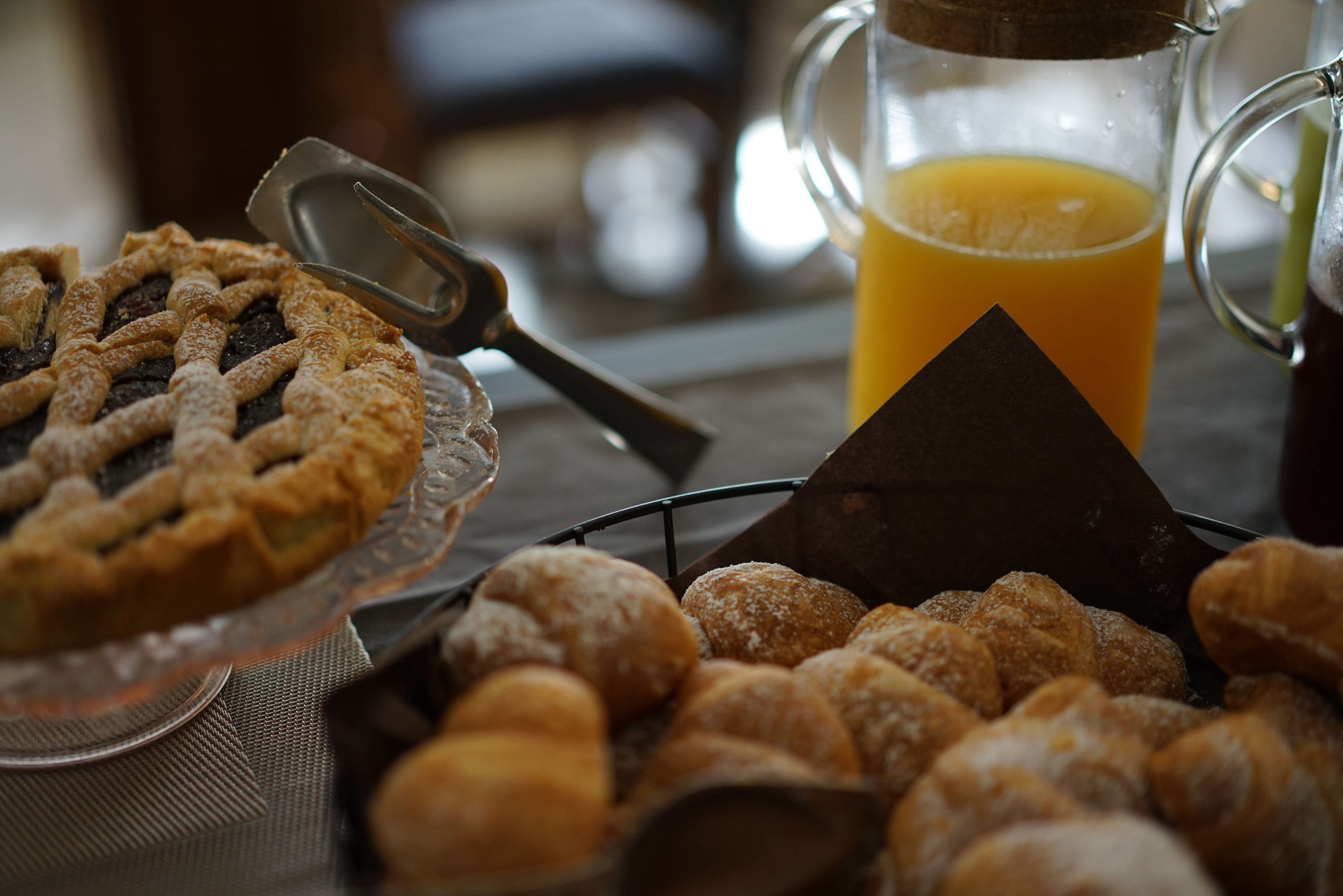A table with a pie, a pitcher of orange juice, and a basket of pastries.