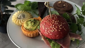 Un plato con tres niveles lleno de pasteles y frutas variadas.