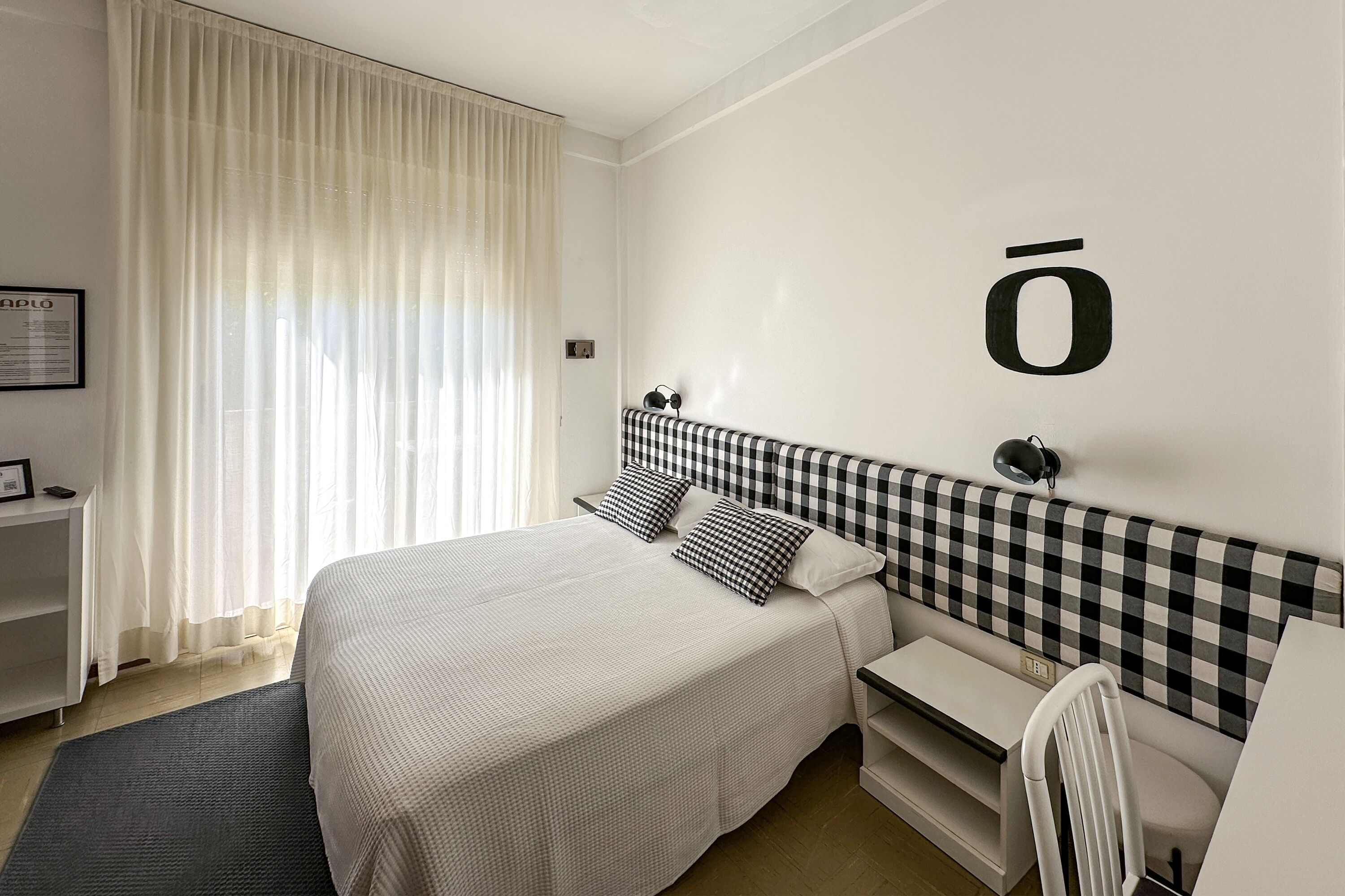 Une chambre d’hôtel bien rangée, avec un lit, une tête de lit à carreaux, un bureau et une chaise.
