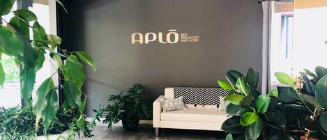 A modern interior with a sofa, potted plants, and a wall with the text "APLO BED BREAKFAST AND MORE".