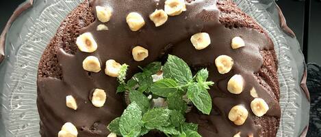 A chocolate cake with hazelnuts and mint leaves on a glass plate.