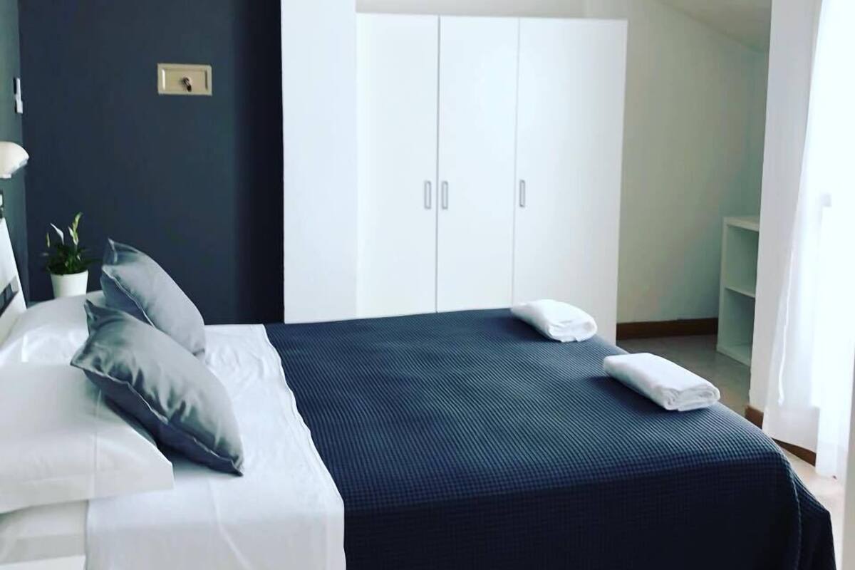 Un dormitorio con cama, mesita de noche, armario y una planta pequeña.