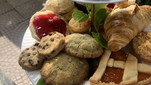 Un plato de diversos pasteles y frutas, incluyendo cruasanes, scones y rebanadas de manzana, con un fondo de mesas al aire libre.