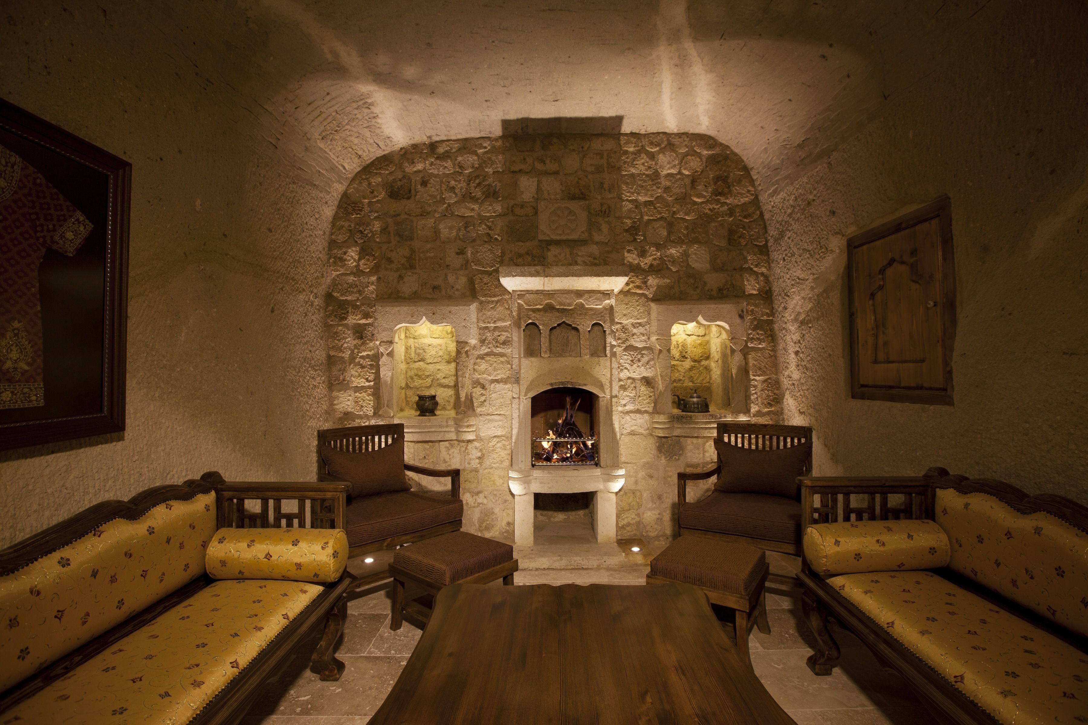 A stone-walled room with a fireplace, wooden furniture, and a framed picture on the wall.