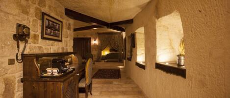A narrow stone corridor with a wooden reception desk, a framed photograph, and a bed in the background.
