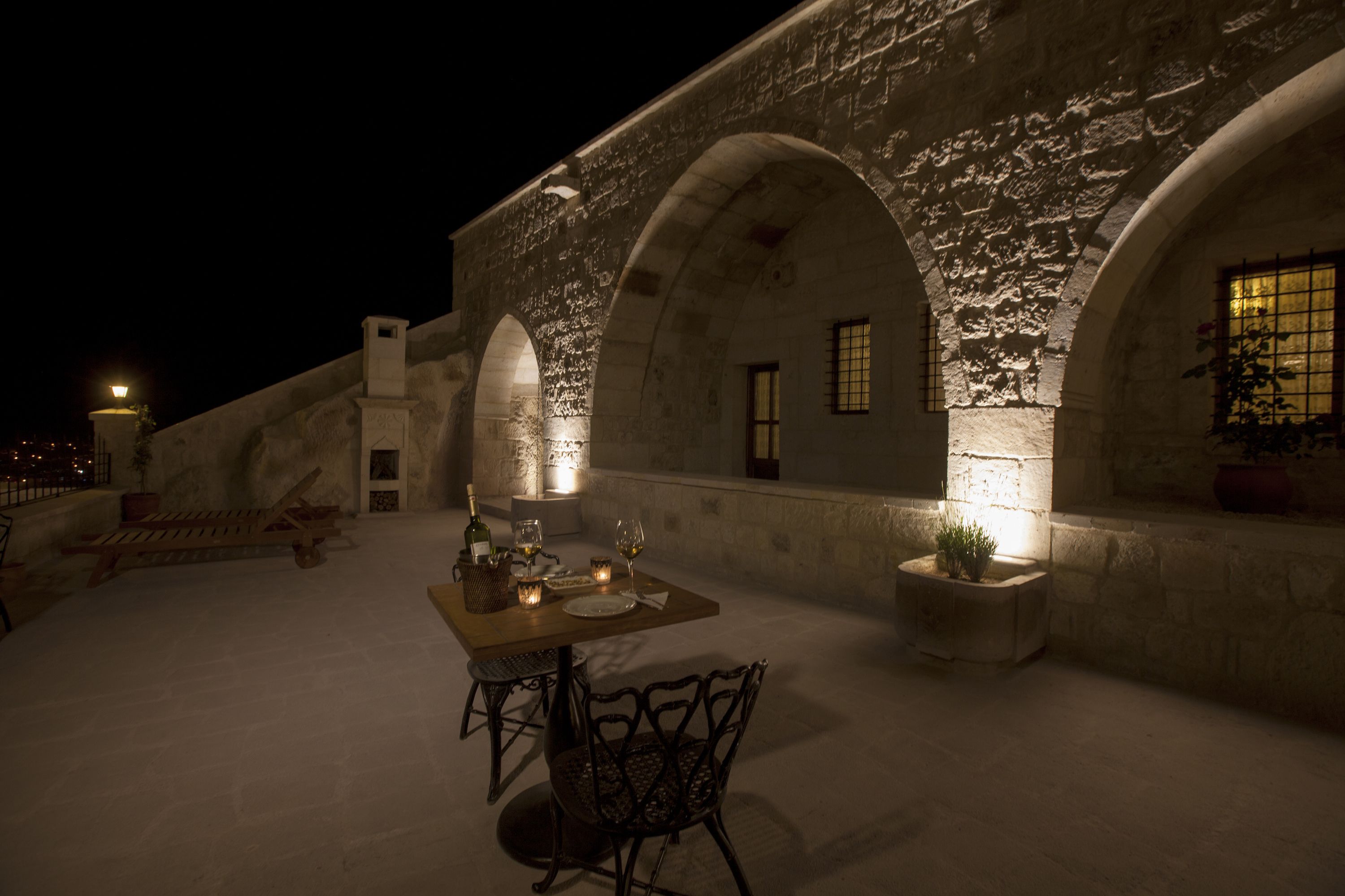 An outdoor dining area with a table set for two, surrounded by stone arches and potted plants.