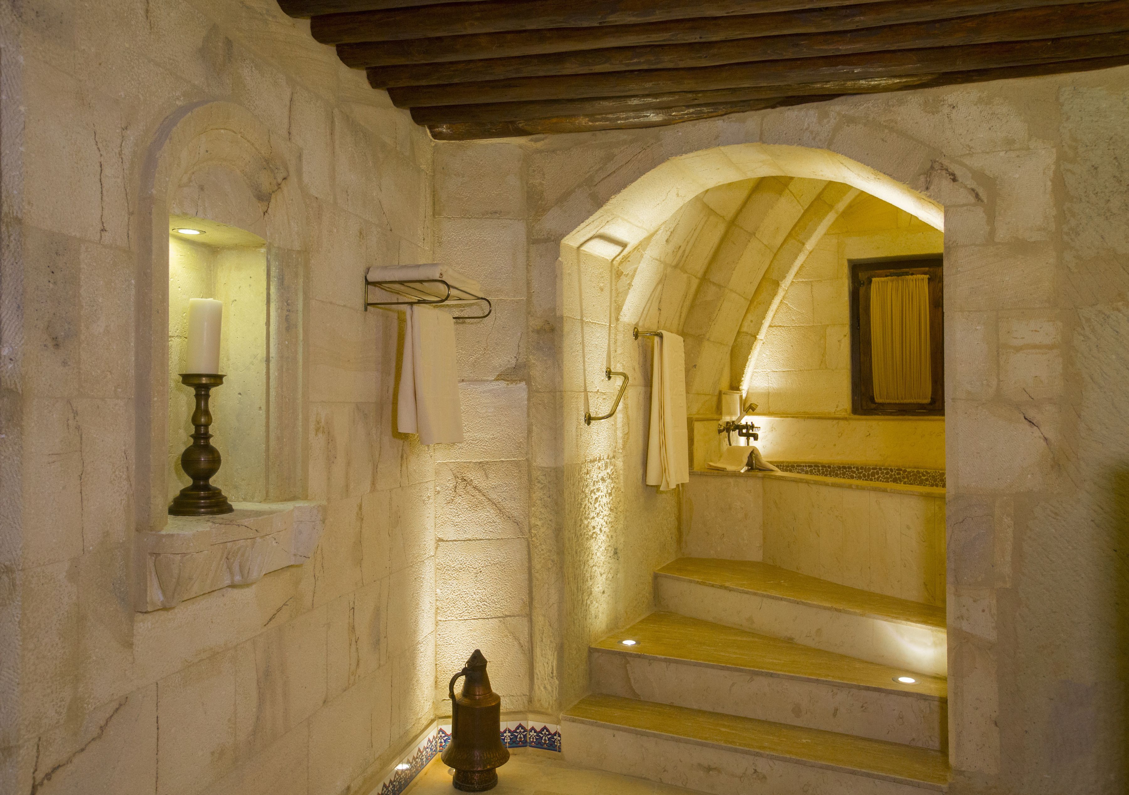 A stone-walled bathroom with a wooden bench, a candle holder, and a mirror.