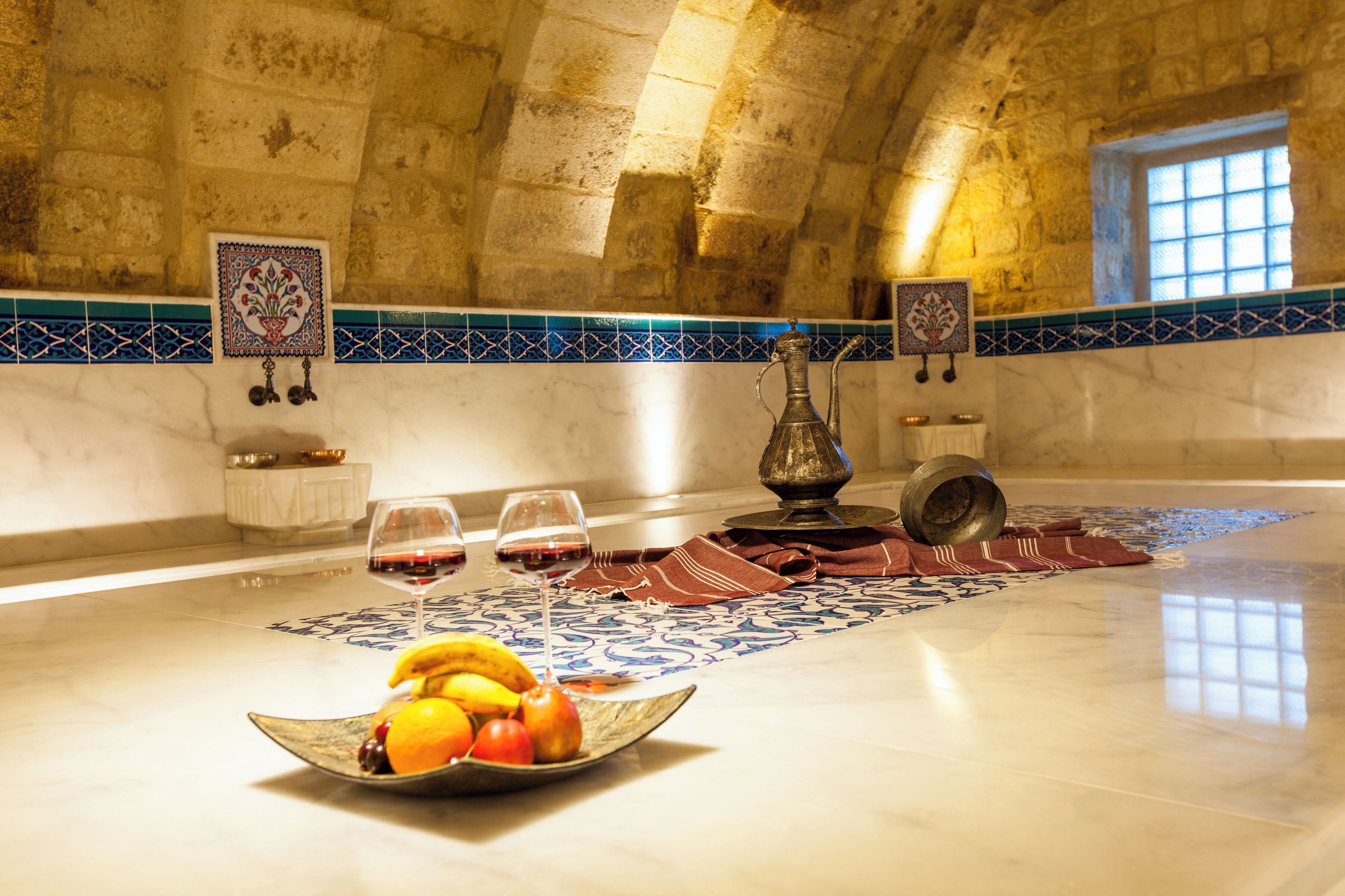 Una habitación con suelo de baldosas, una mesa con fruta y copas de vino, y un cuenco decorativo.