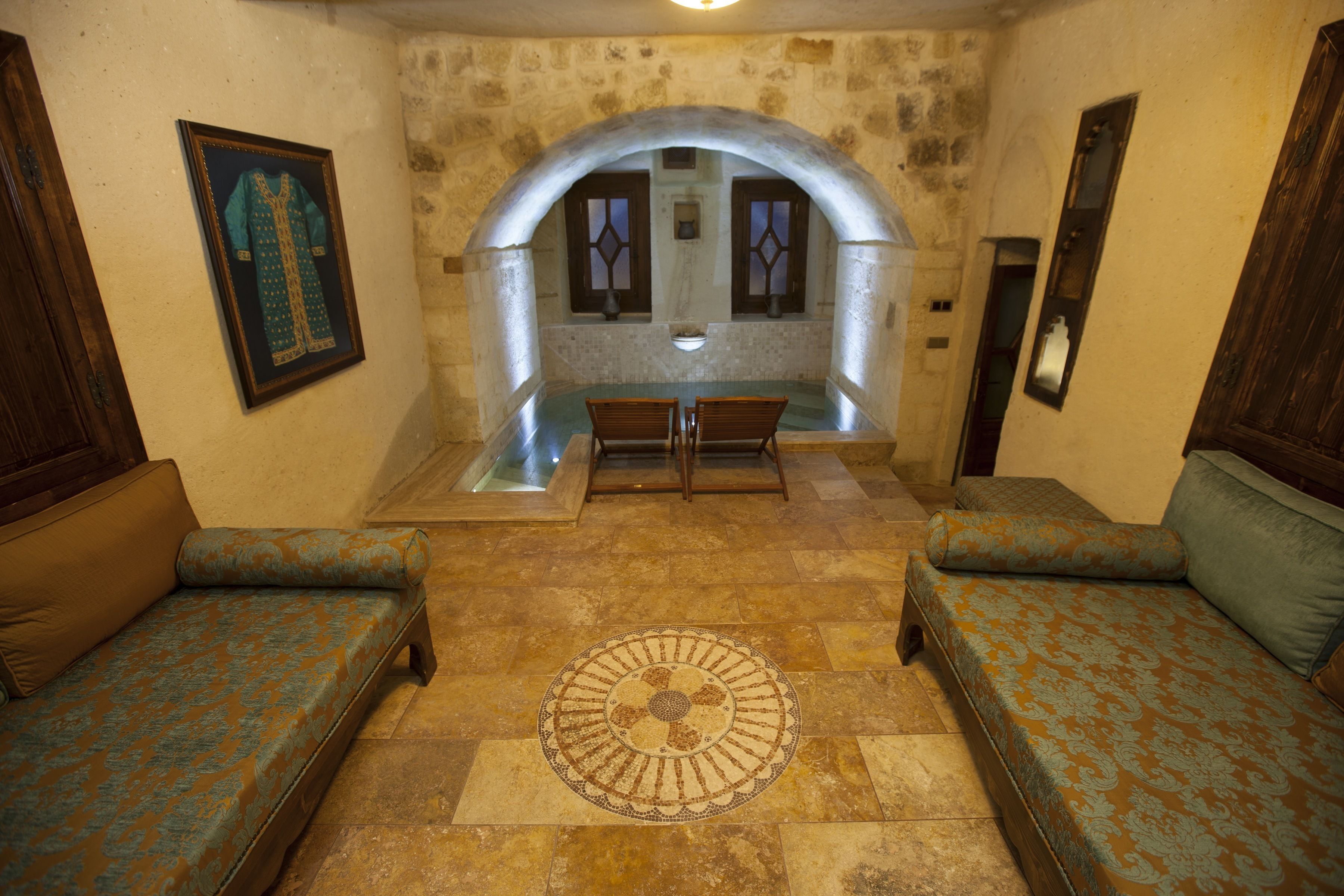 A room with a stone wall, a wooden bench, a patterned rug, and a framed picture on the wall.