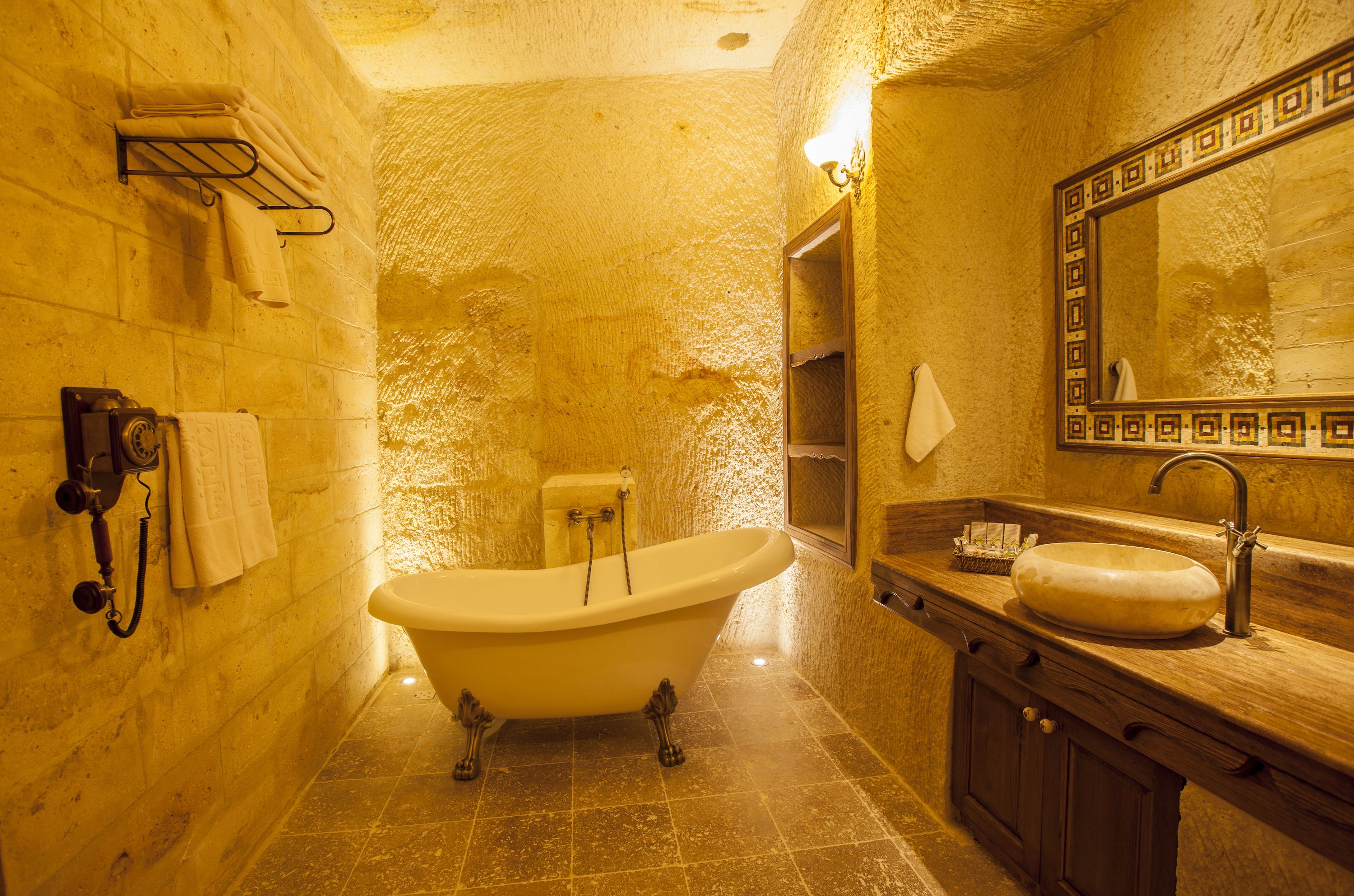 Un baño con una bañera independiente, un tocador de madera con lavamanos y un espejo grande con marco decorativo.