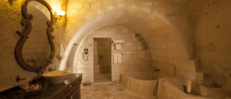 A stone-walled bathroom with a freestanding bathtub, a sink, and a large mirror.