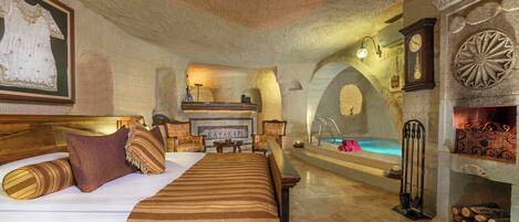 A spacious bedroom with a large bed, a fireplace, a hot tub, and a wooden headboard.
