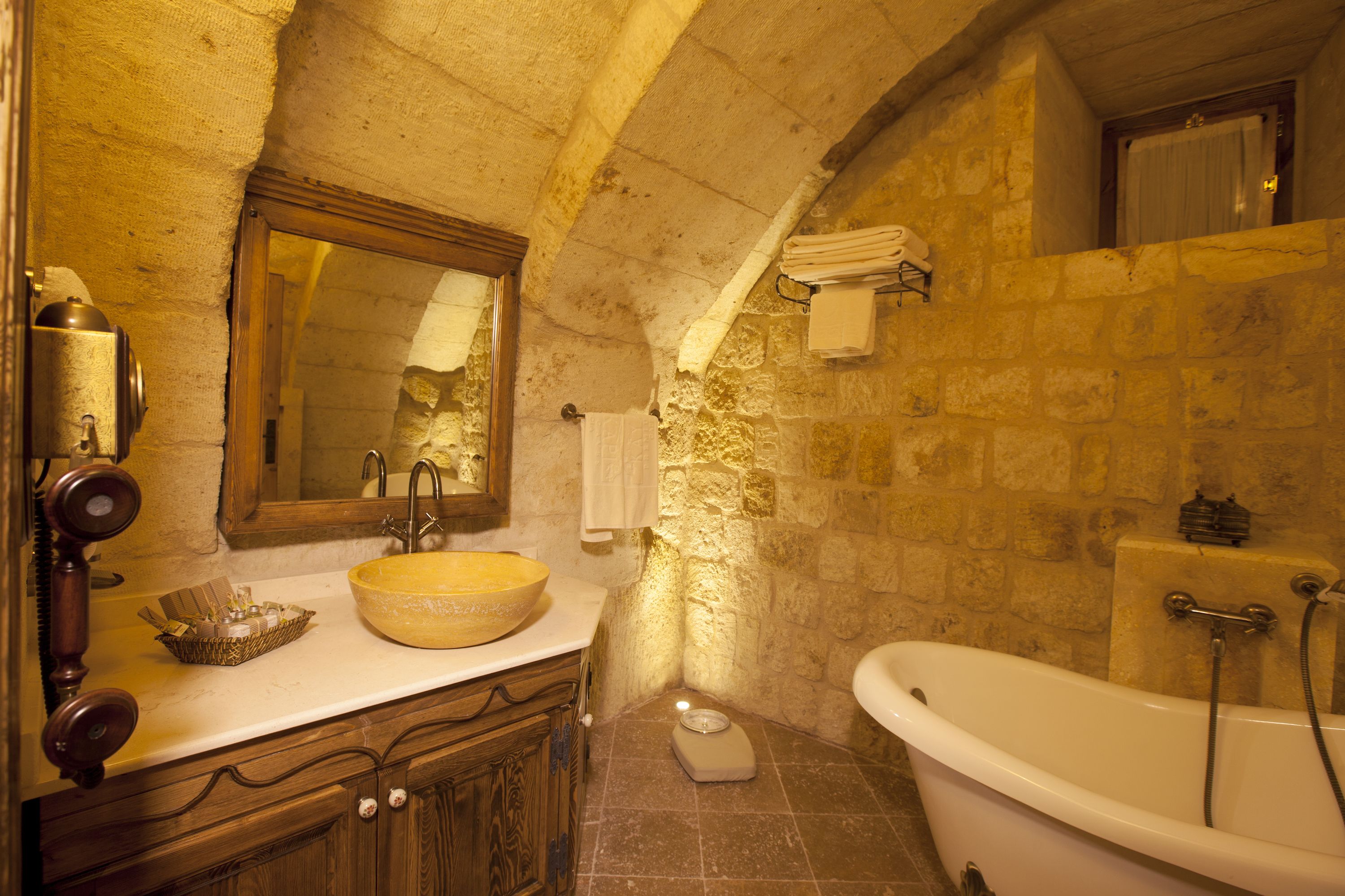 Un baño con pared de piedra, tocador de madera, un lavabo grande y una bañera.