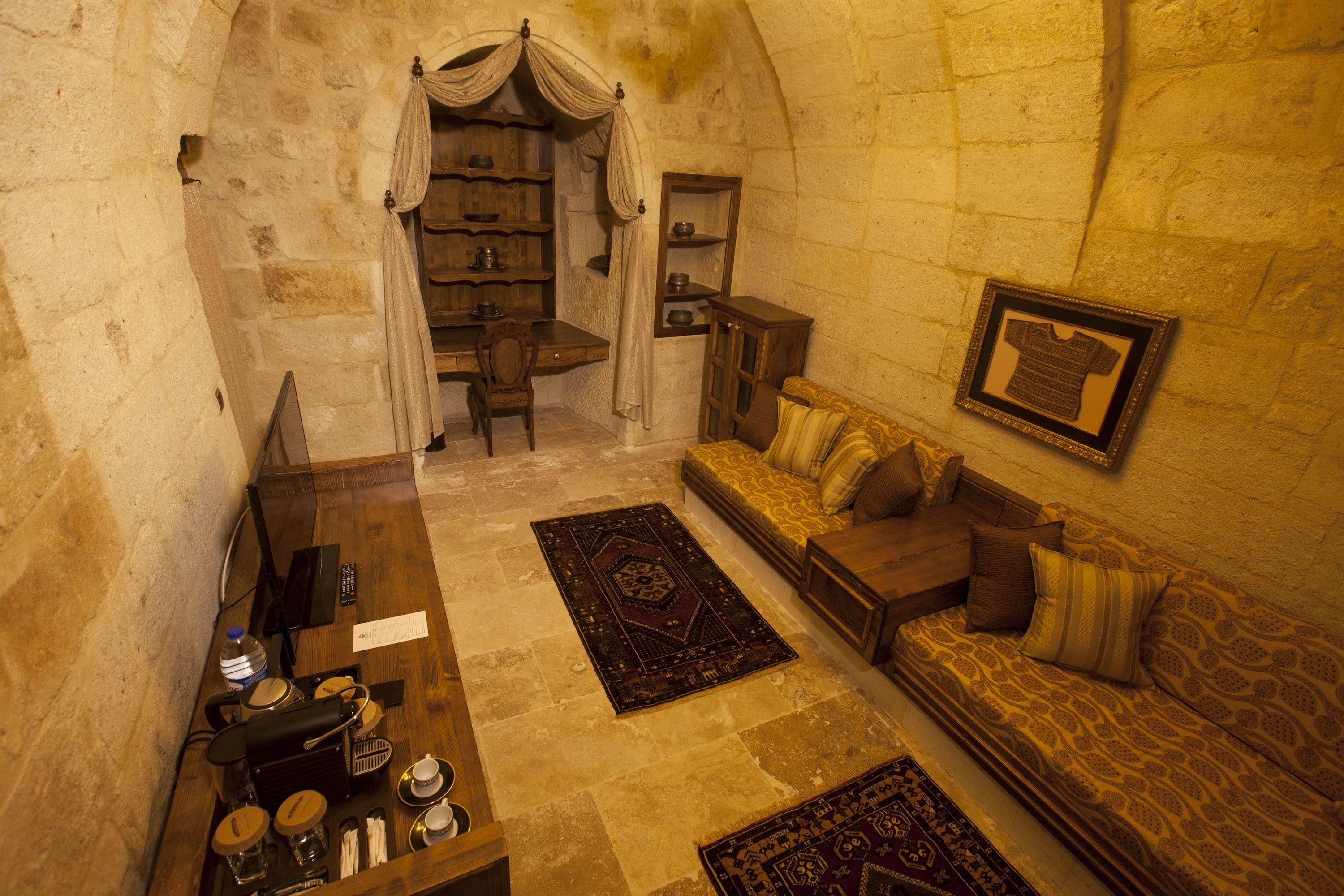 A cozy room with a wooden desk, a sofa, and a patterned rug. There is a small table with a water bottle and a remote control.