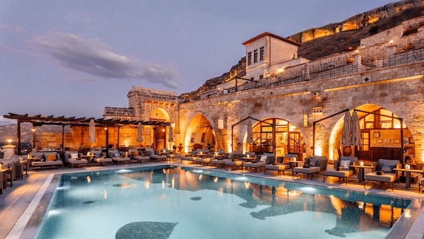 A pool area with lounge chairs and a stone building with arches. - Kayakapi Premium Caves - Cappadocia (Ürgüp)