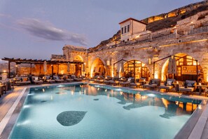 Un área de piscina con sillones de descanso y un edificio de piedra con arcos.