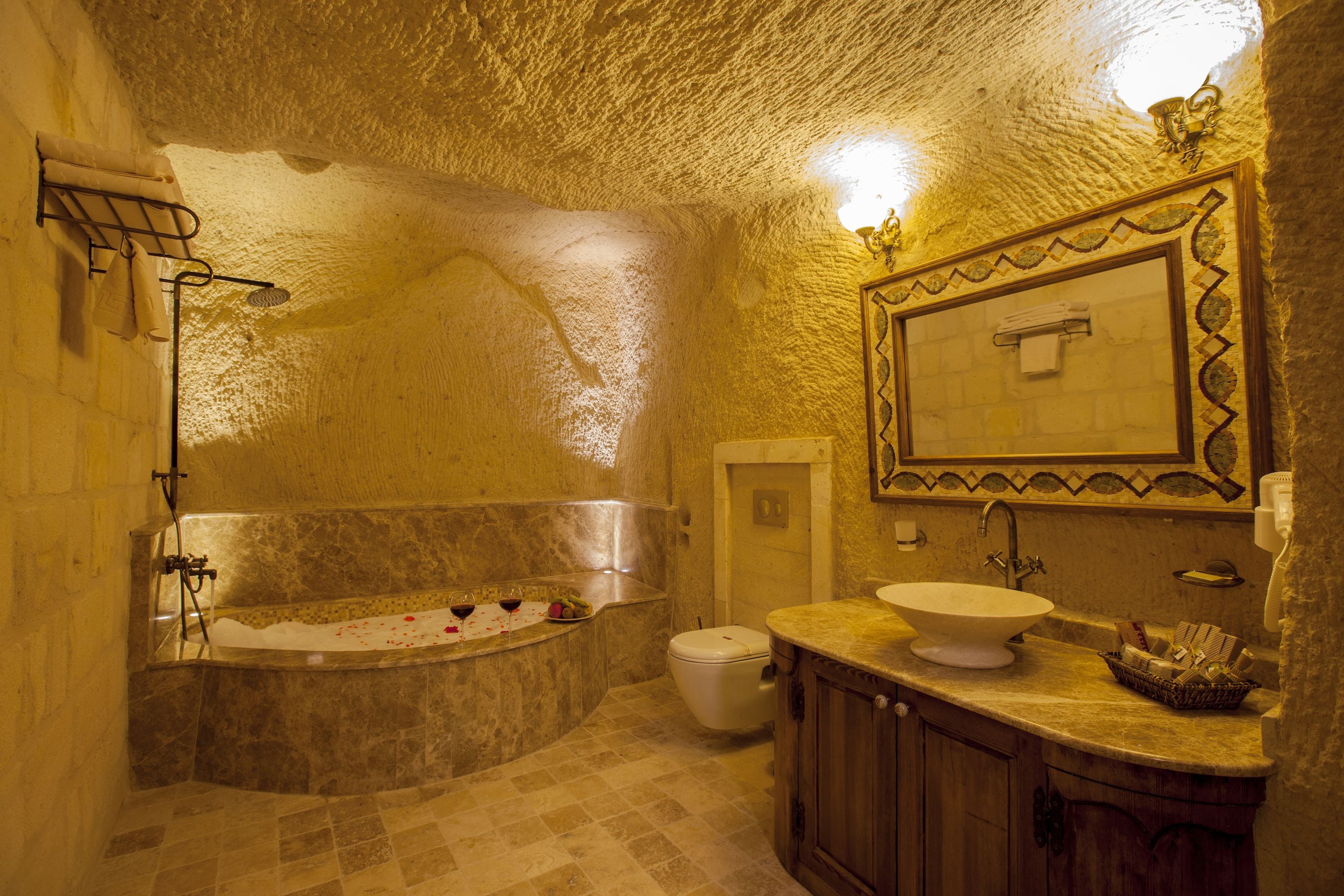 A bathroom with a stone wall, a bathtub, a toilet, and a sink with a mirror above it.