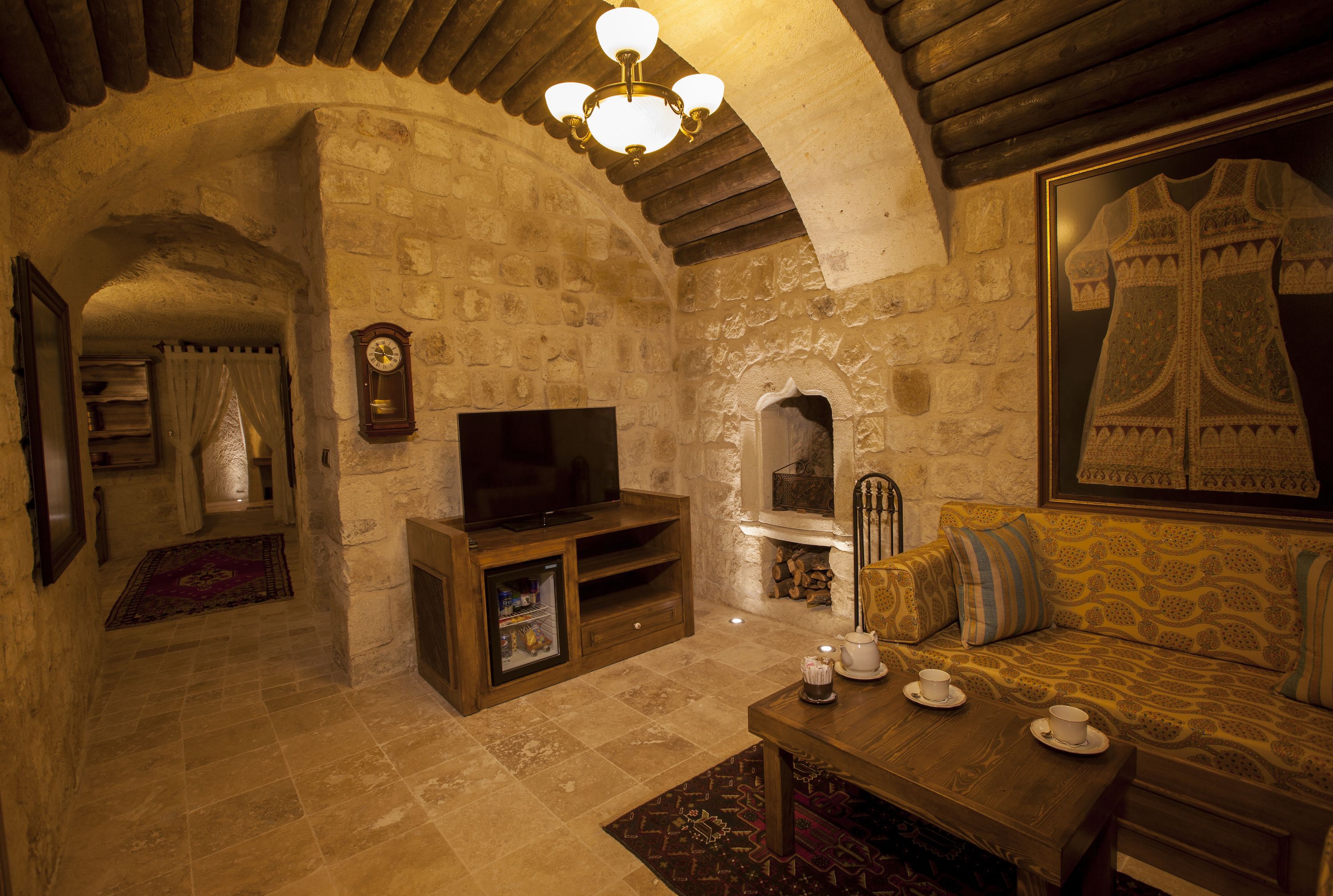 Una habitación acogedora con paredes de piedra, techo de madera, chimenea, sofá, televisor y candelabro.